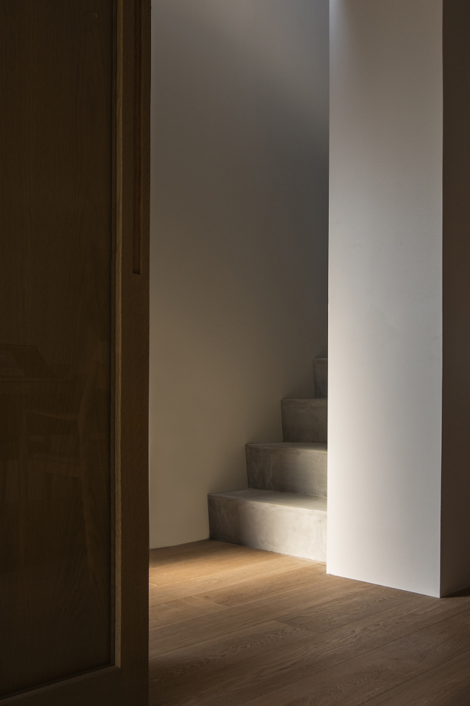 An out-of-view opening shines a small amount of light on the bottom concrete steps of a stairway. The rest of the stairs is shadowed.