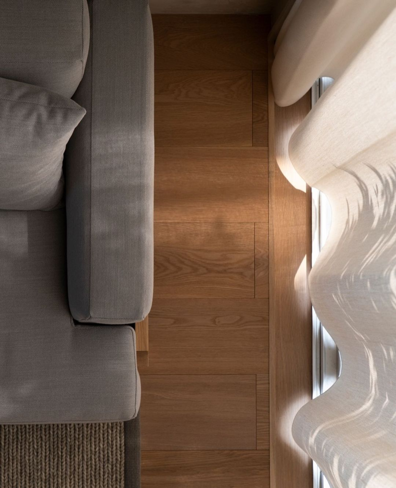Overhead photograph of wooden floorboards running between a grey couch and white curtain