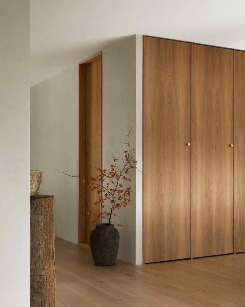 Floor to ceiling wooden cabinet doors line a wall, next to a black urn decorated with black branches