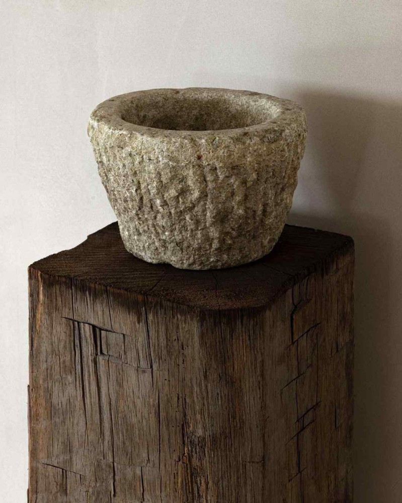 A rough-cut stone bowl placed on the square top of a weathered wood pedestal
