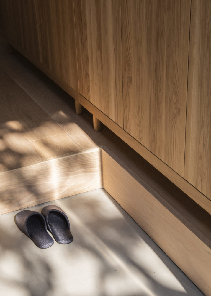 Speckled light falls into an entryway with a grey concrete floor and warm wood cabinets