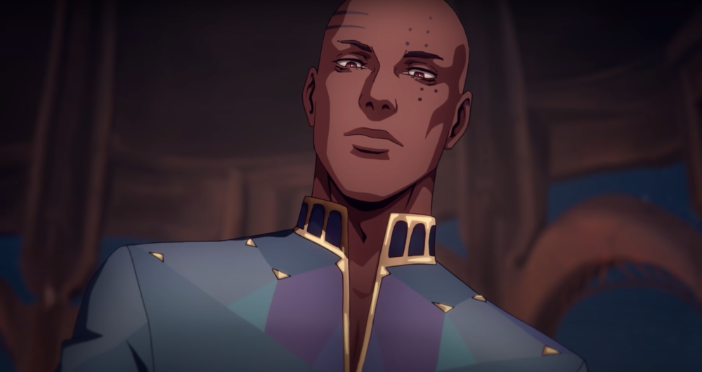 Screengrab of a handsome longfaced black man gazing pensively downwards towards the camera. He'd bald, and there are dark markings on his face. He's wearing a simple but princely shirt that's coloured in blues and purples with gold lining.