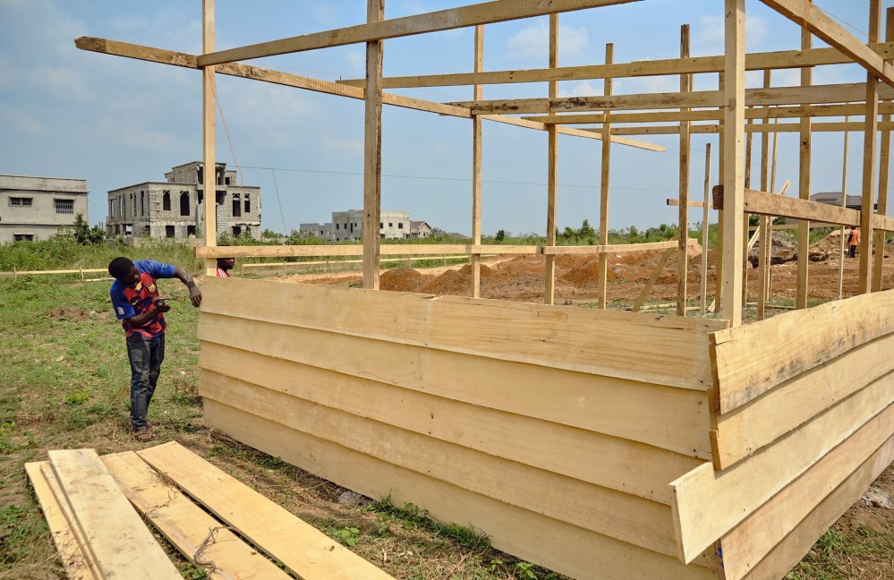 A gentleman nails rough-hewn planks of wood for the temporary site office