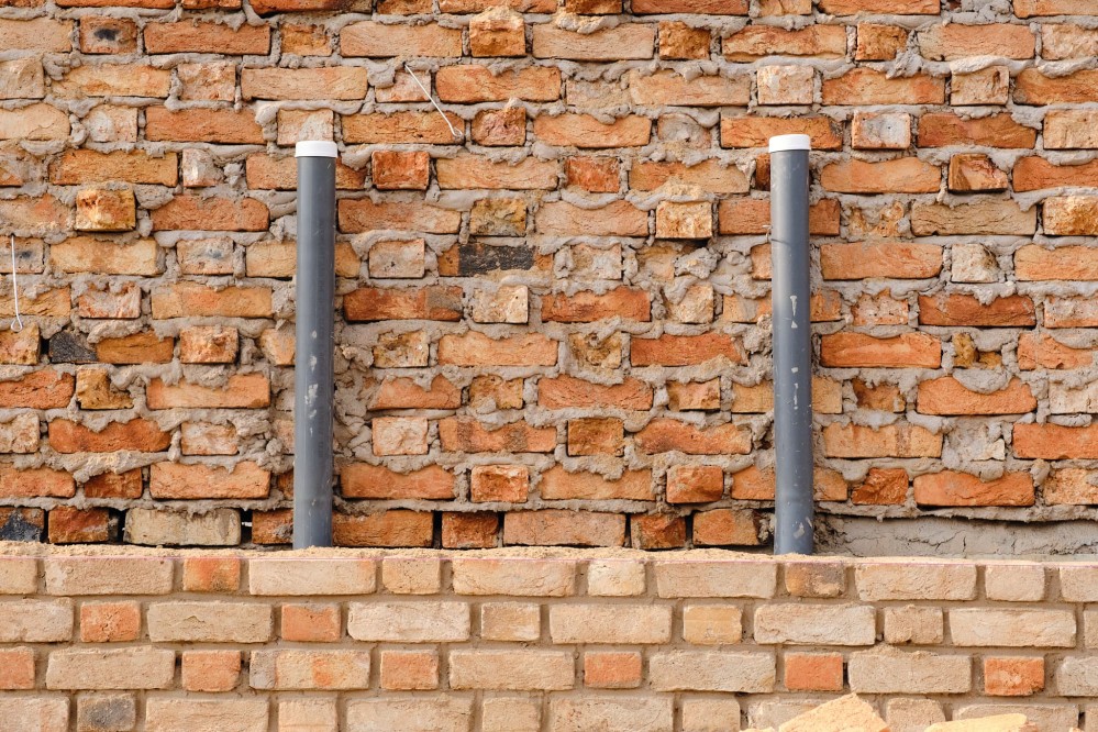 Two grey pipes running three-quarters up the side of a brick wall