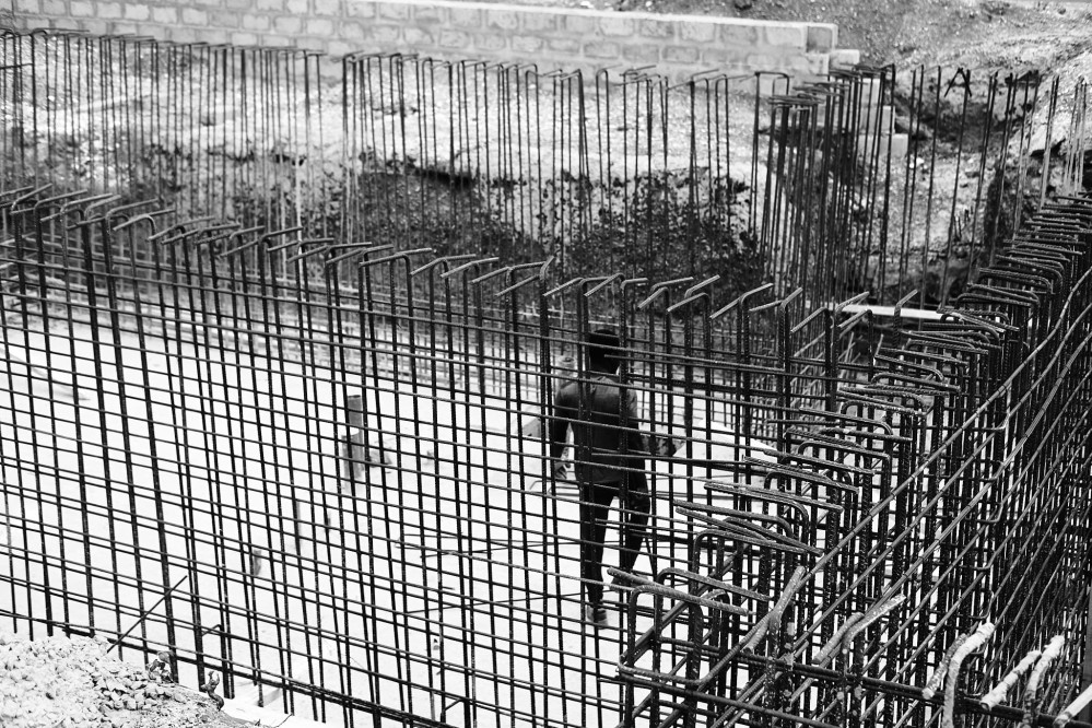 A man walks across the bottom of the excavation, surrounded by iron rods