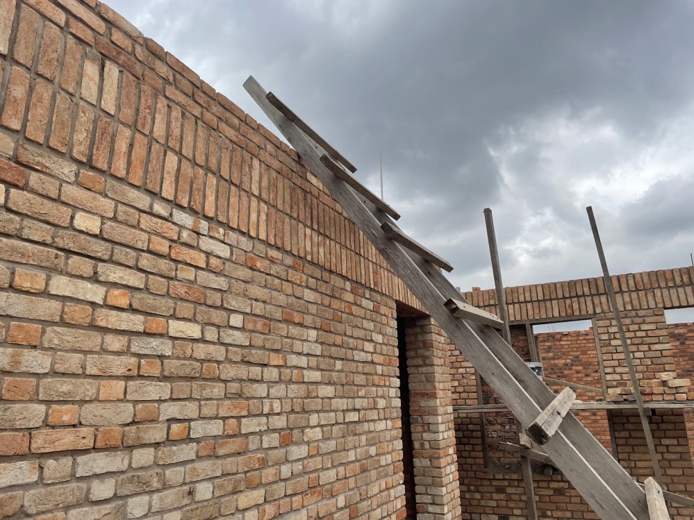 A wood ladder leans against the roofline of a brick building