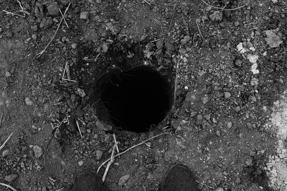 Black and white close-up of a dark fist-sized hole in the earth.