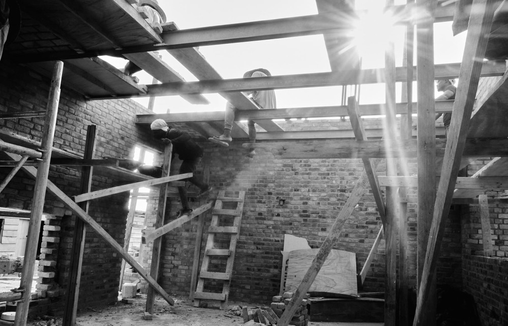 Sunlight streams through the open ceiling of a brick room under construction