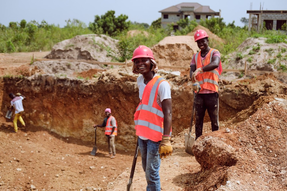 Smiling workers pause from working on the excavation to strike a pose while leaning against their shovels