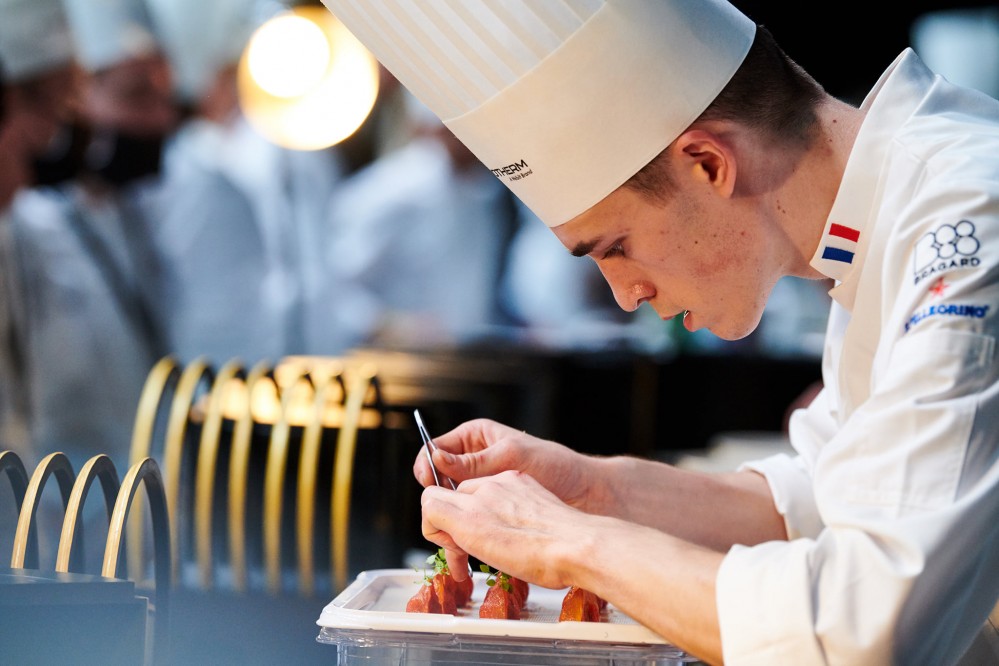 A young chef uses a pair of tweezers to plate