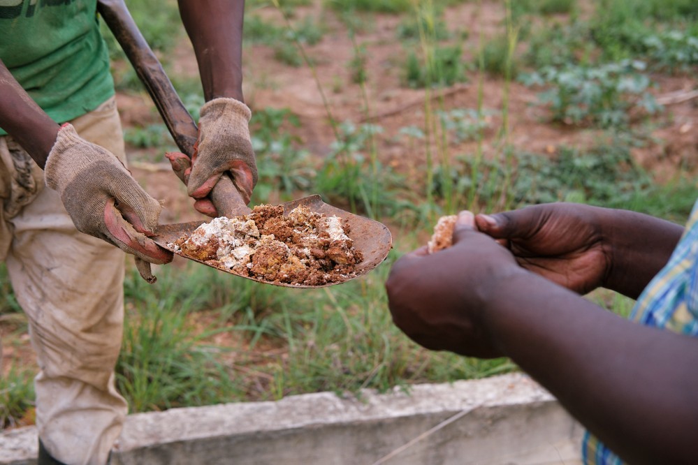 One man holds up a shovel full of soil and another appears to be breaking it between his fingers, testing for something