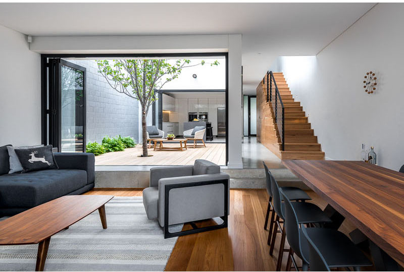 Living area with warm orange wood floors. The room wraps around and open courtyard which is accessed by a high step. The courtyard has a wooden floor, with a small tree growing through it.